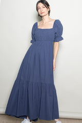 woman wearing a navy blue maxi dress with puff sleeves and a tiered skirt, standing against a neutral backdrop