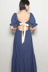 woman wearing a navy blue dress with puff sleeves and an open back featuring a tied bow detail
