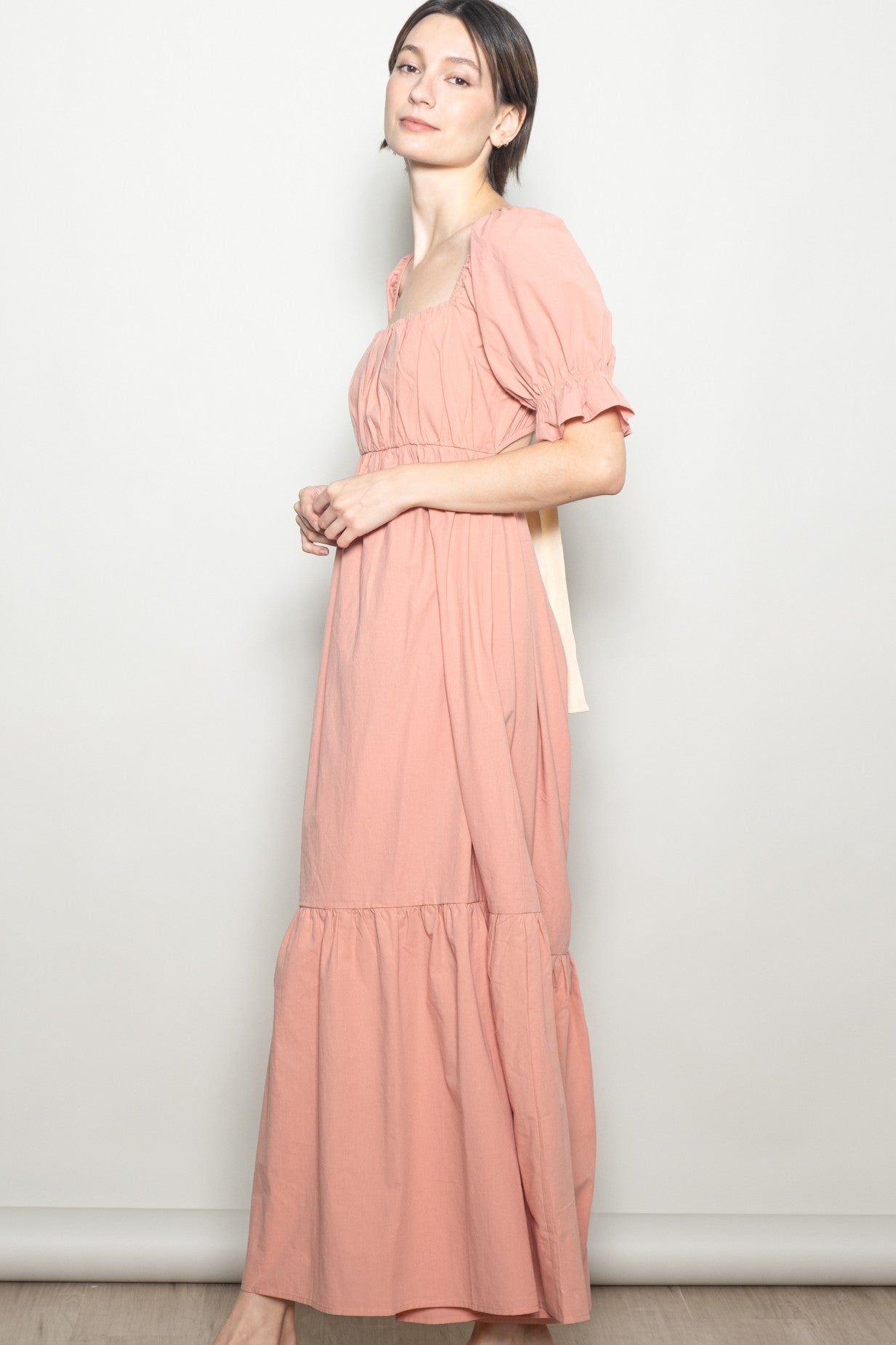 woman wearing a pink maxi dress with a square neckline and puff sleeves, standing sideways against a light background