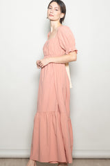 woman wearing a pink maxi dress with a square neckline and puff sleeves, standing sideways against a light background
