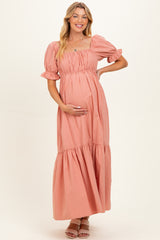 woman wearing a pink maternity maxi dress with puff sleeves and a tiered skirt, holding her baby bump