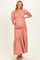 woman wearing a pink maternity maxi dress with puff sleeves and a tiered skirt, holding her baby bump