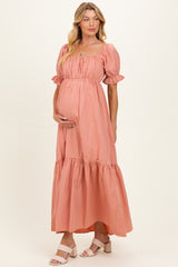 woman wearing a peach maternity maxi dress with puffed sleeves and ruffled hem, gently cradling her baby bump