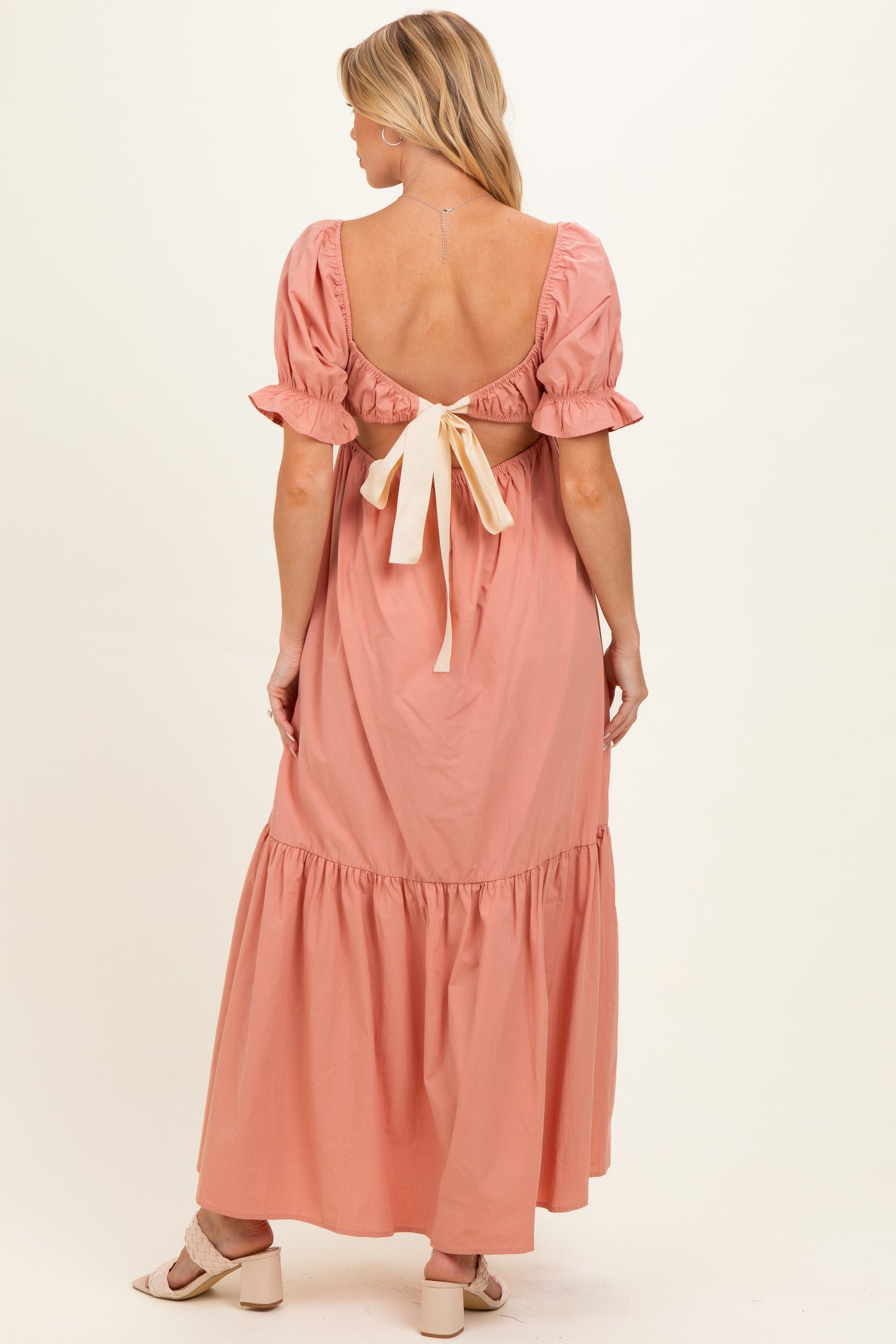 woman wearing a light pink maternity maxi dress with puff sleeves and a tied back detail