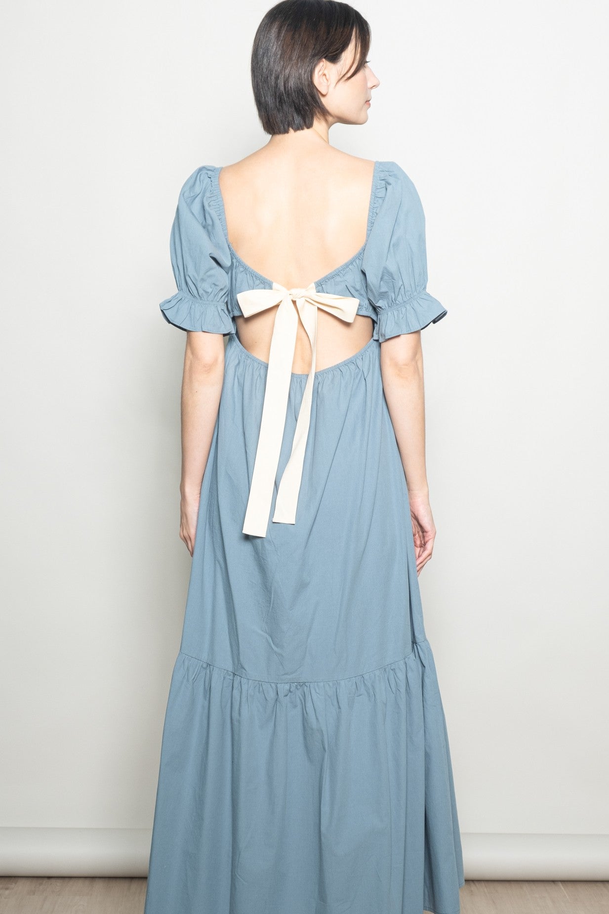 woman wearing a backless blue maxi dress with puff sleeves and a bow detail at the back