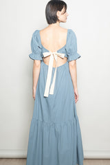 woman wearing a backless blue maxi dress with puff sleeves and a bow detail at the back