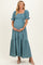 woman wearing a teal maternity maxi dress with puff sleeves and a tiered skirt, holding her baby bump