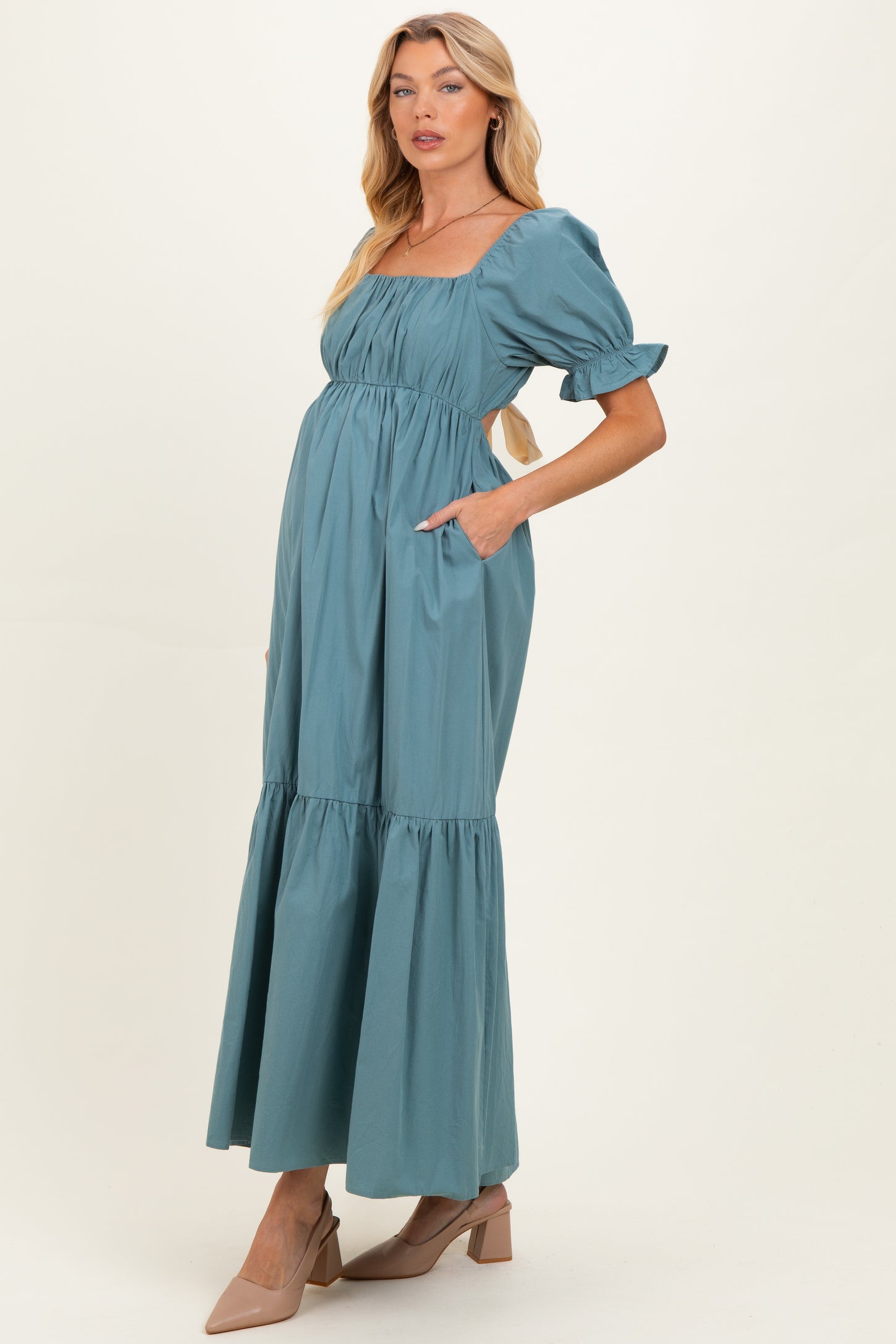 woman wearing a teal maternity maxi dress with puff sleeves and pockets, featuring a square neckline and tiered hem
