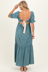 woman wearing a teal maternity maxi dress with a cut-out back and puff sleeves, showing a stylish bow detail