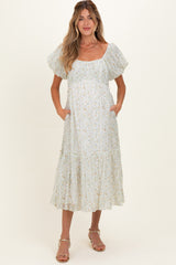 woman wearing a floral maternity dress with puff sleeves and pockets, styled with a tiered skirt