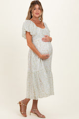 woman wearing a light blue floral maternity dress and holding her baby bump