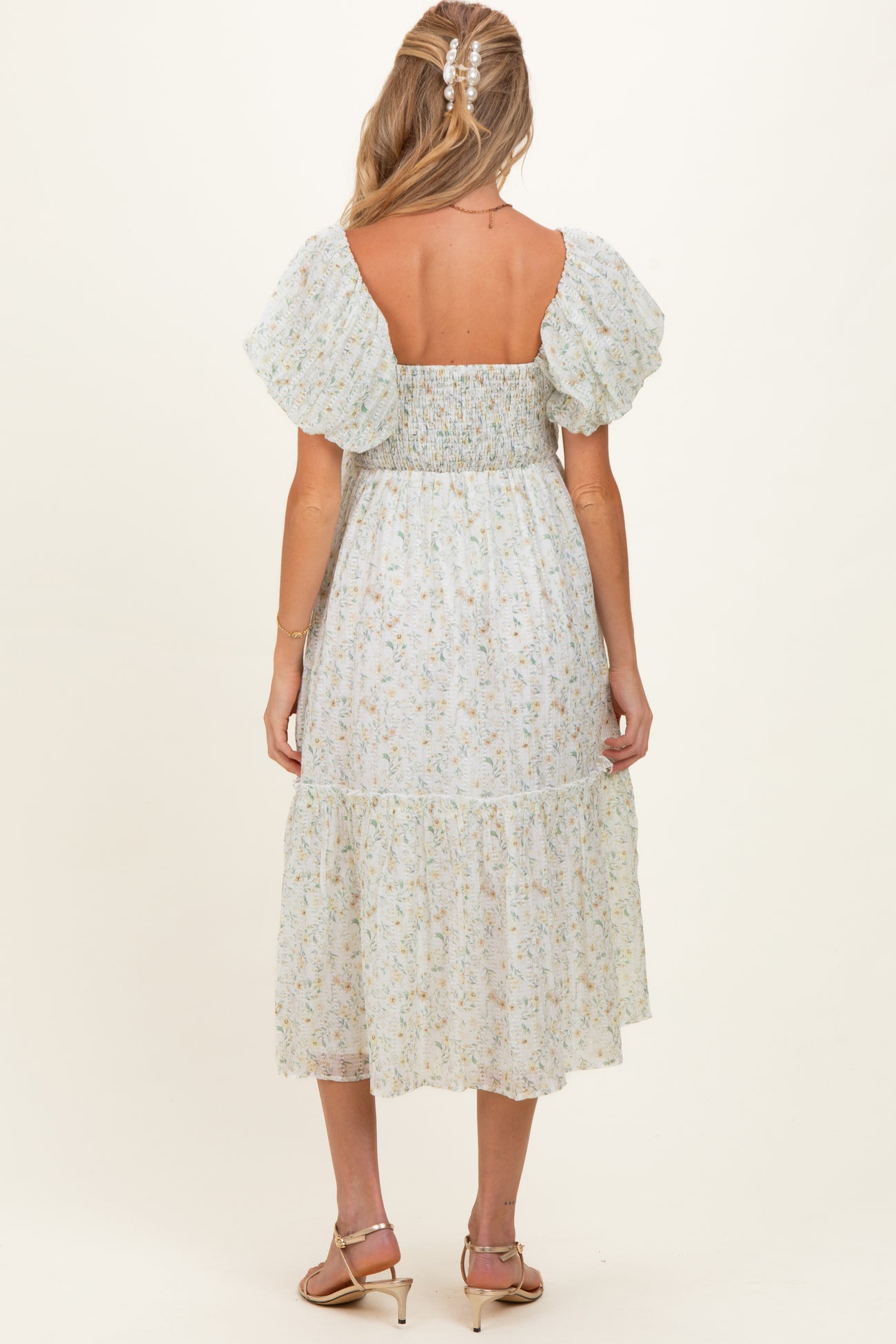 woman wearing a light blue floral maternity dress with puff sleeves and a tiered skirt, showing a baby bump