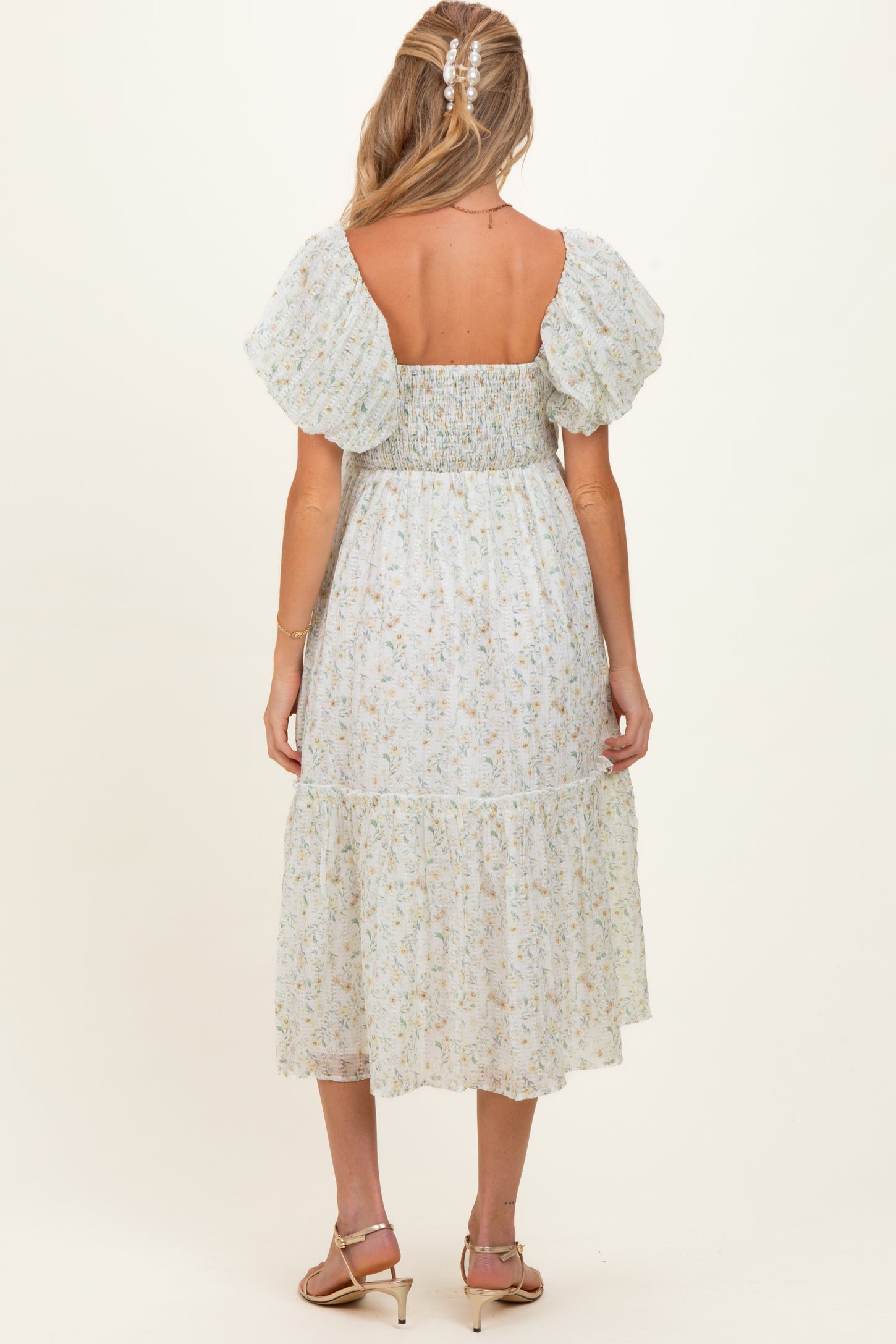 woman wearing a light blue floral maternity dress with puff sleeves and a tiered skirt, showing a baby bump