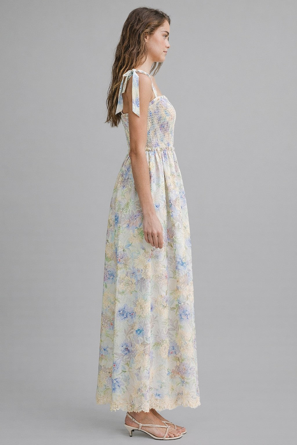 woman wearing a floral maxi dress with adjustable tie straps and a smocked bodice in pastel colors