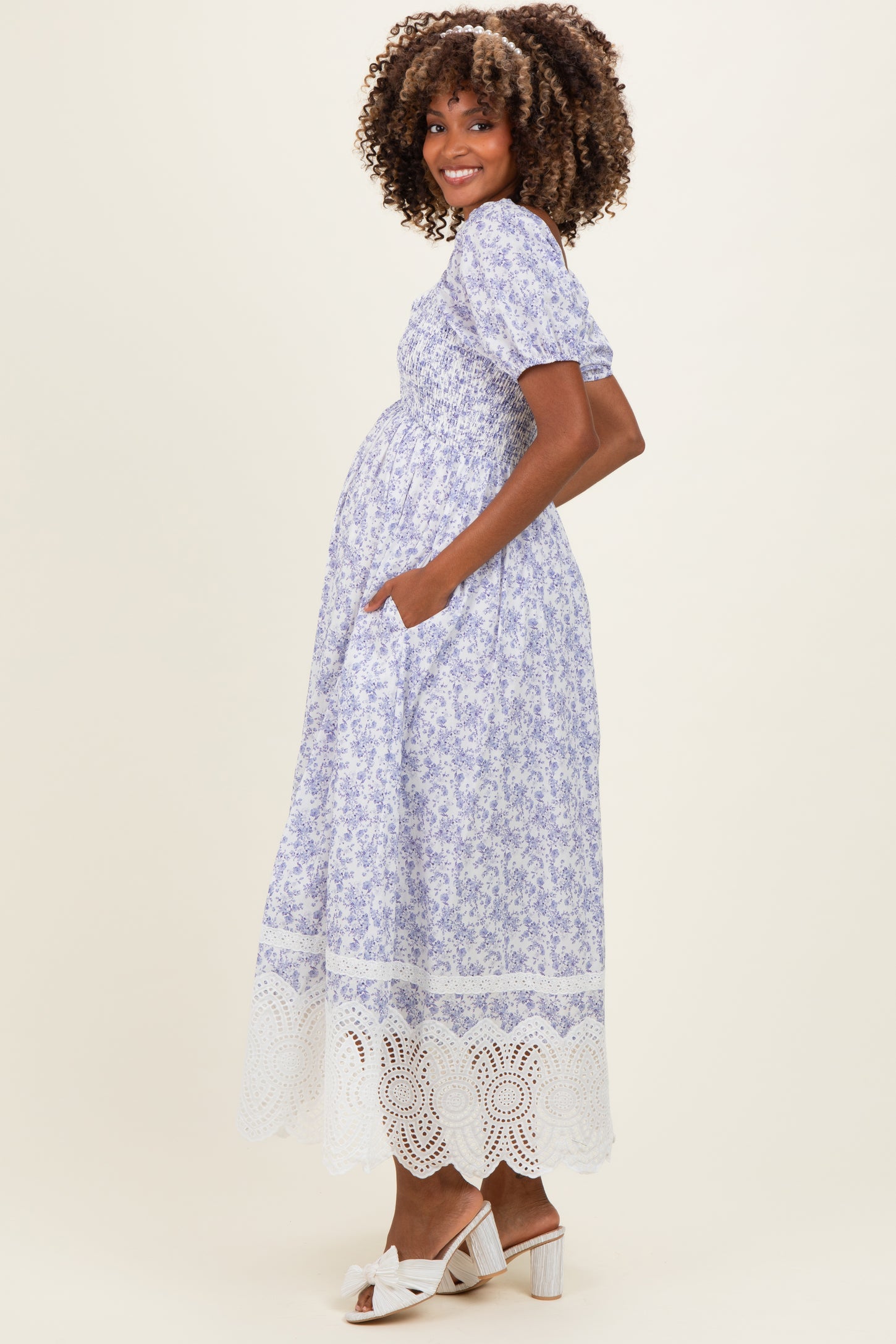 woman wearing a lavender floral maternity dress with puff sleeves and lace hem, showing her baby bump and standing sideways