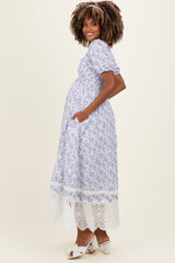 woman wearing a lavender floral maternity dress with puff sleeves and lace hem, showing her baby bump and standing sideways