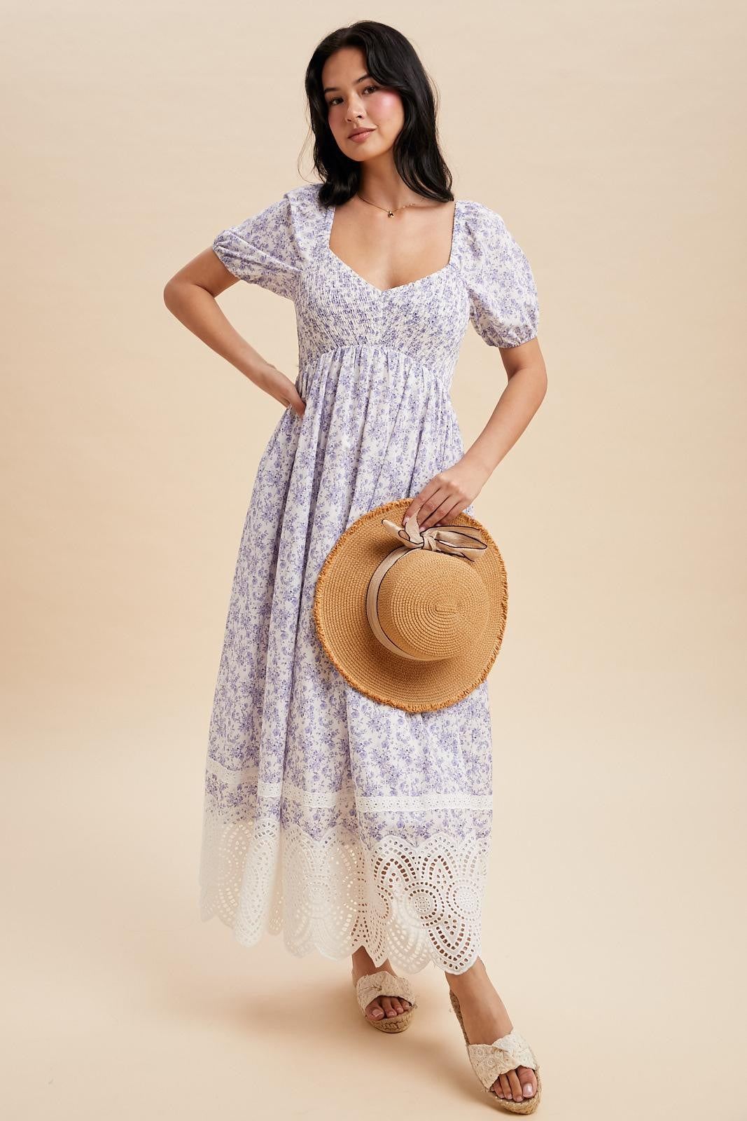 woman wearing a lavender floral maxi dress with puff sleeves and lace trim, holding a straw hat