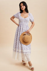 woman wearing a lavender floral maxi dress with puff sleeves and lace trim, holding a straw hat