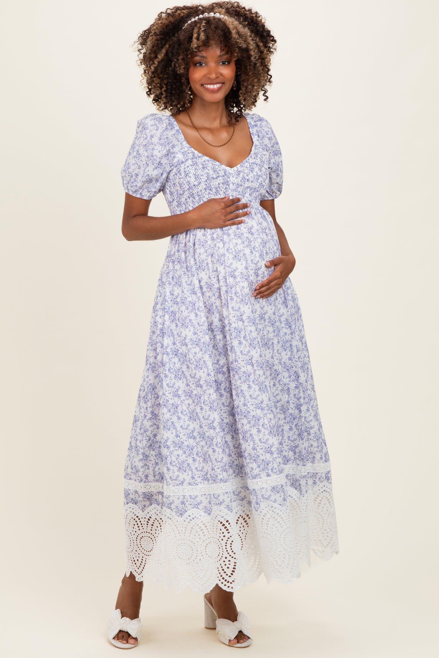 woman wearing a maternity maxi dress with a floral print and lace hemline, holding her baby bump