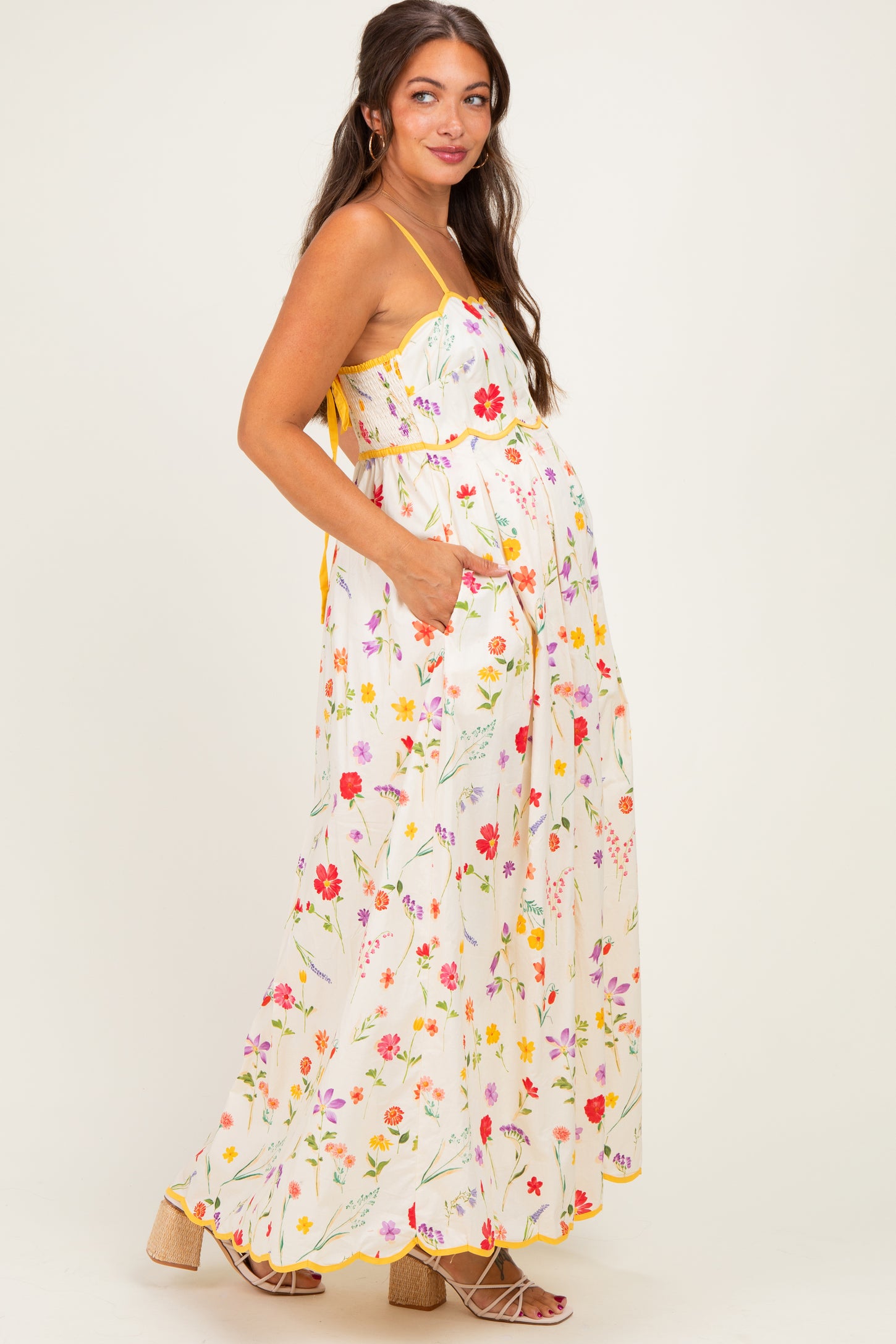 woman wearing a white floral maternity maxi dress with pockets and a yellow trim, showing her baby bump