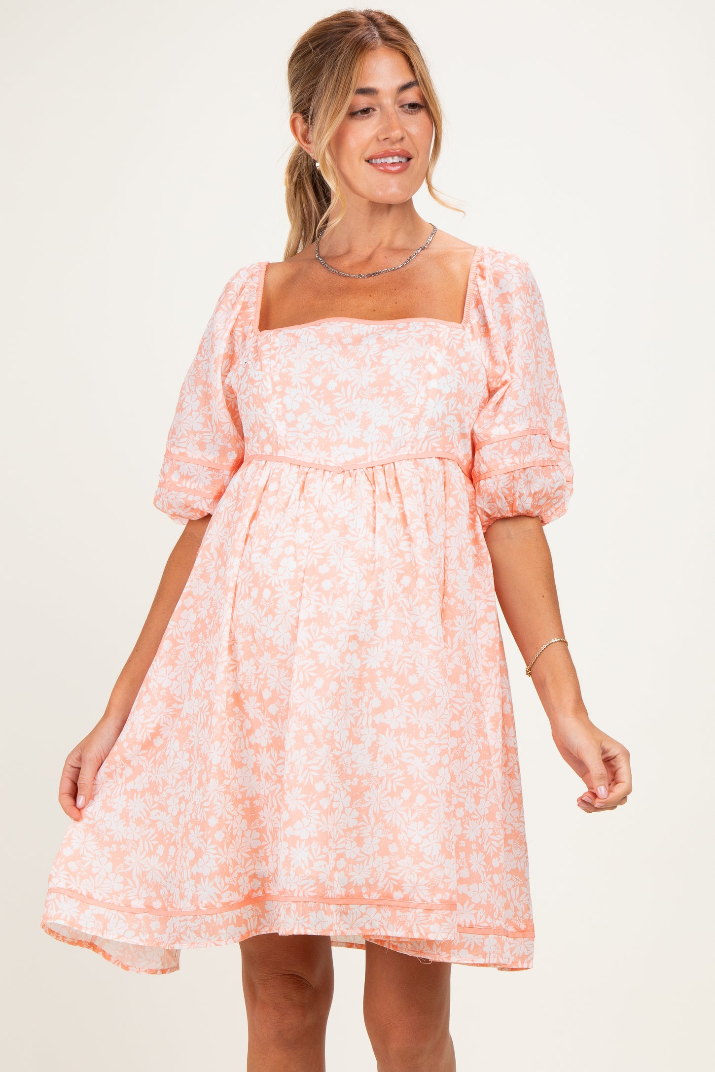 woman wearing a maternity wear light pink floral puff sleeve dress and showing her baby bump