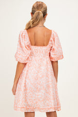 woman wearing a peach floral maternity dress with puff sleeves and a smocked back detail