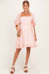 woman wearing a pink floral maternity dress with puff sleeves and a square neckline, holding a small bag