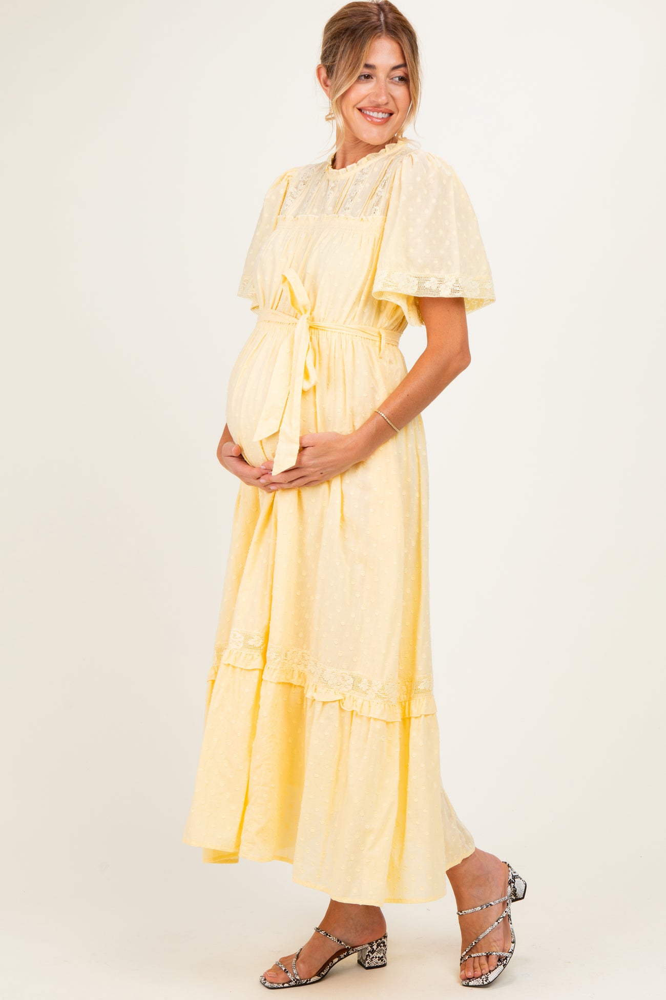 woman wearing a yellow maternity dress with puff sleeves and lace details, holding her baby bump