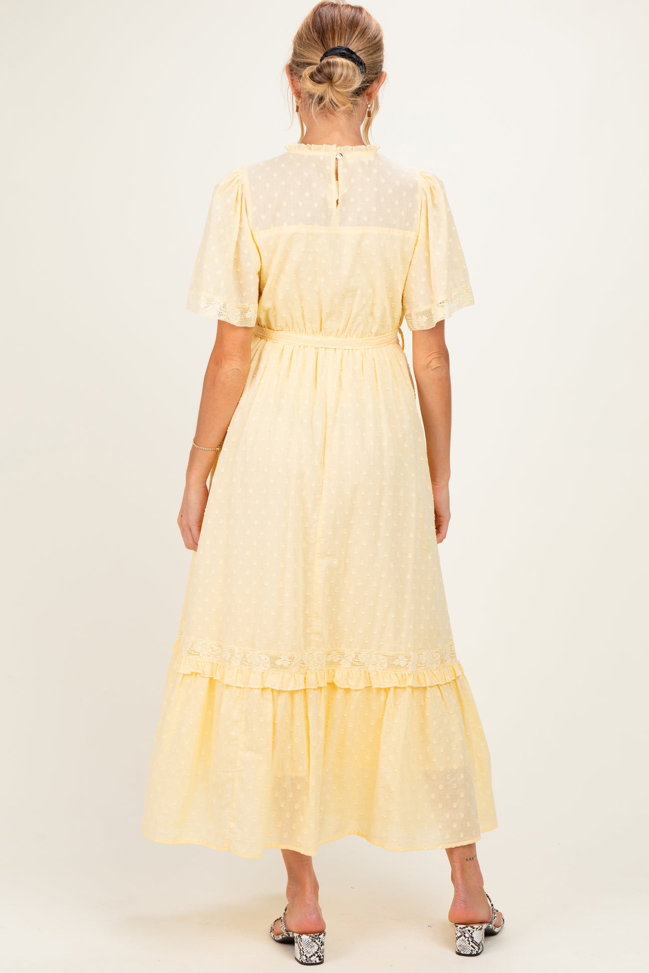 woman wearing a yellow maternity dress with short sleeves and a tiered skirt, viewed from the back