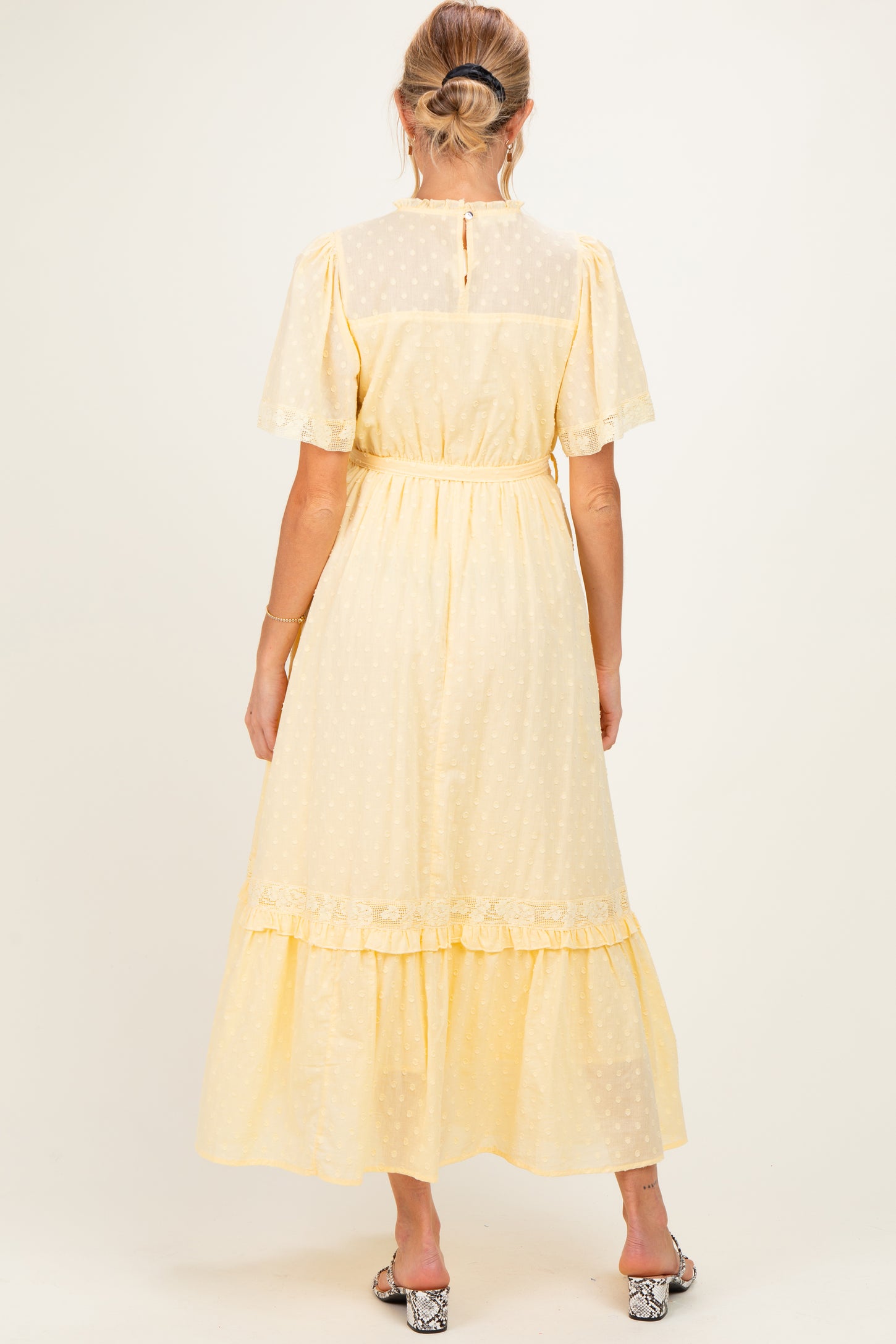 woman wearing a yellow maternity dress with short sleeves and a tiered skirt, viewed from the back