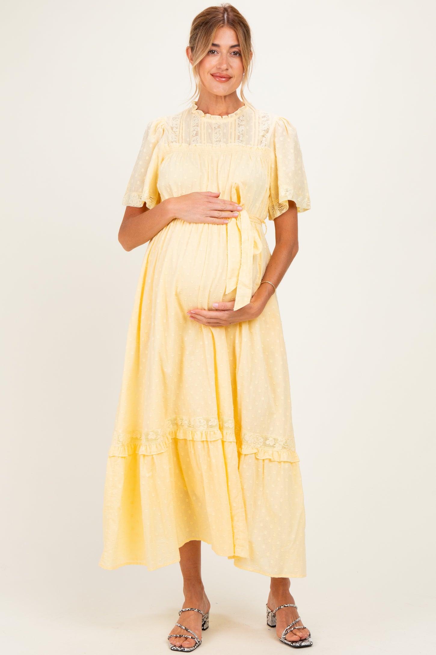 woman wearing a yellow maternity dress with short puff sleeves and a tie at the waist, holding her baby bump