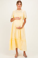 woman wearing a yellow maternity dress with short puff sleeves and a tie at the waist, holding her baby bump