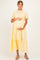 woman wearing a yellow maternity dress with short puff sleeves and a tie at the waist, holding her baby bump