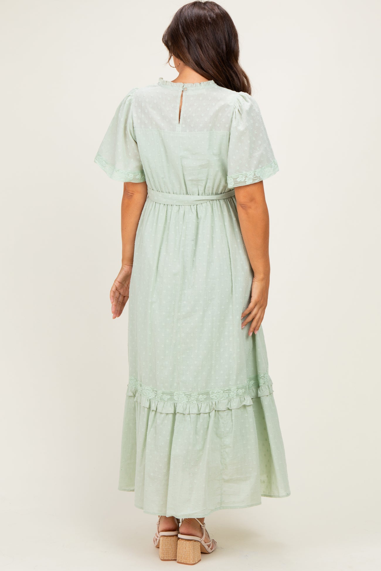 woman wearing a mint green maternity maxi dress with ruffle details and short flutter sleeves, showing the back view