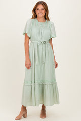 woman wearing a mint green midi dress with flutter sleeves and a tie waist, standing and smiling