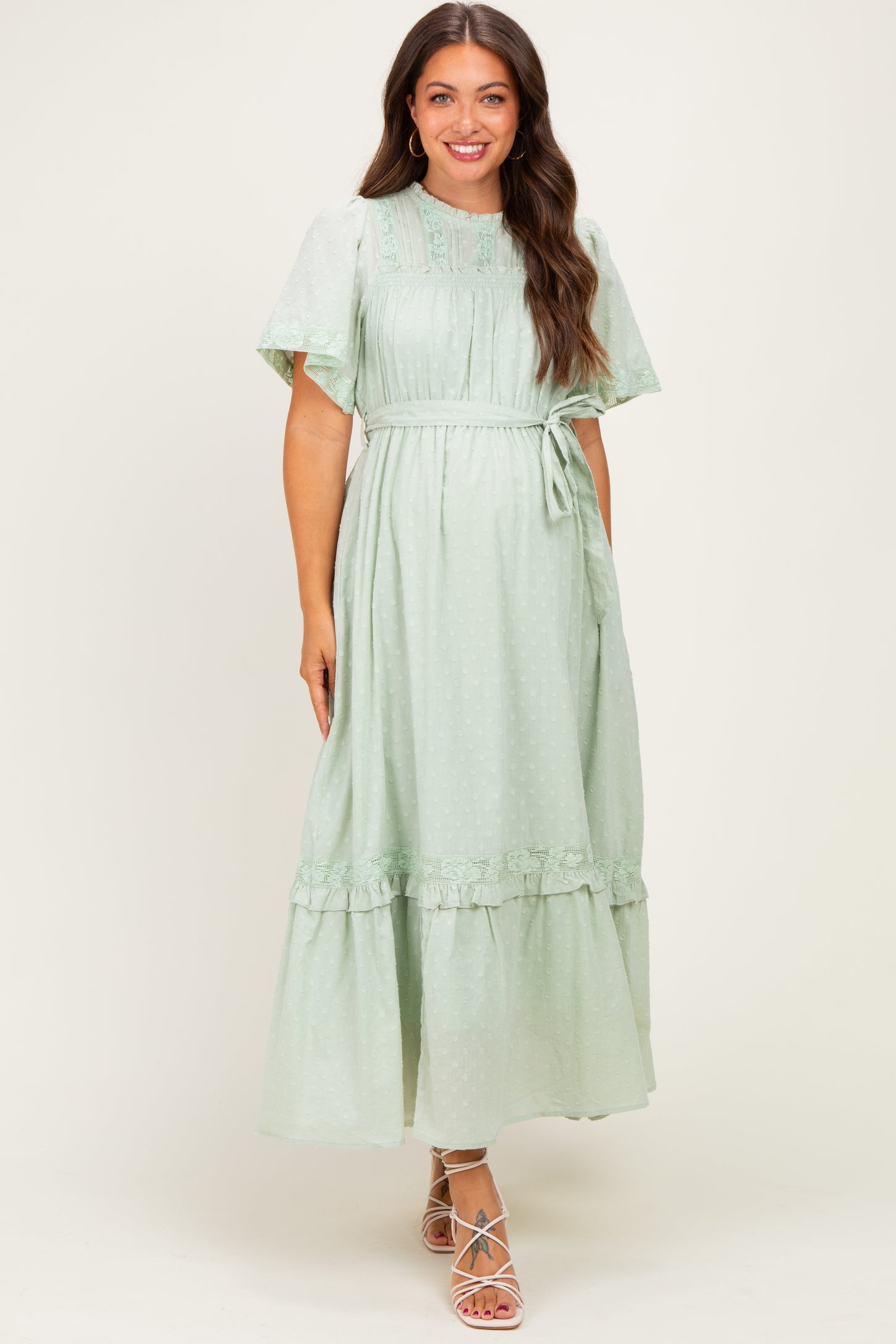 woman wearing a light green maternity maxi dress with short ruffled sleeves and a tie waist detail