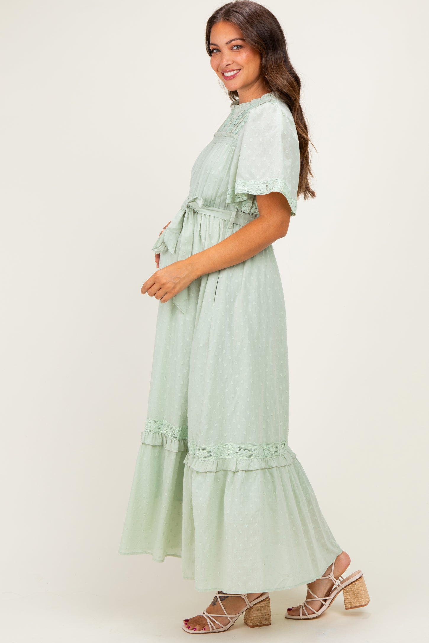 woman wearing a light green maternity dress with ruffle details and a tie waist, showing her baby bump