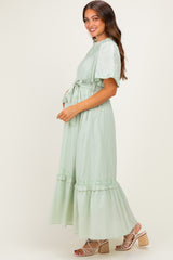woman wearing a light green maternity dress with ruffle details and a tie waist, showing her baby bump