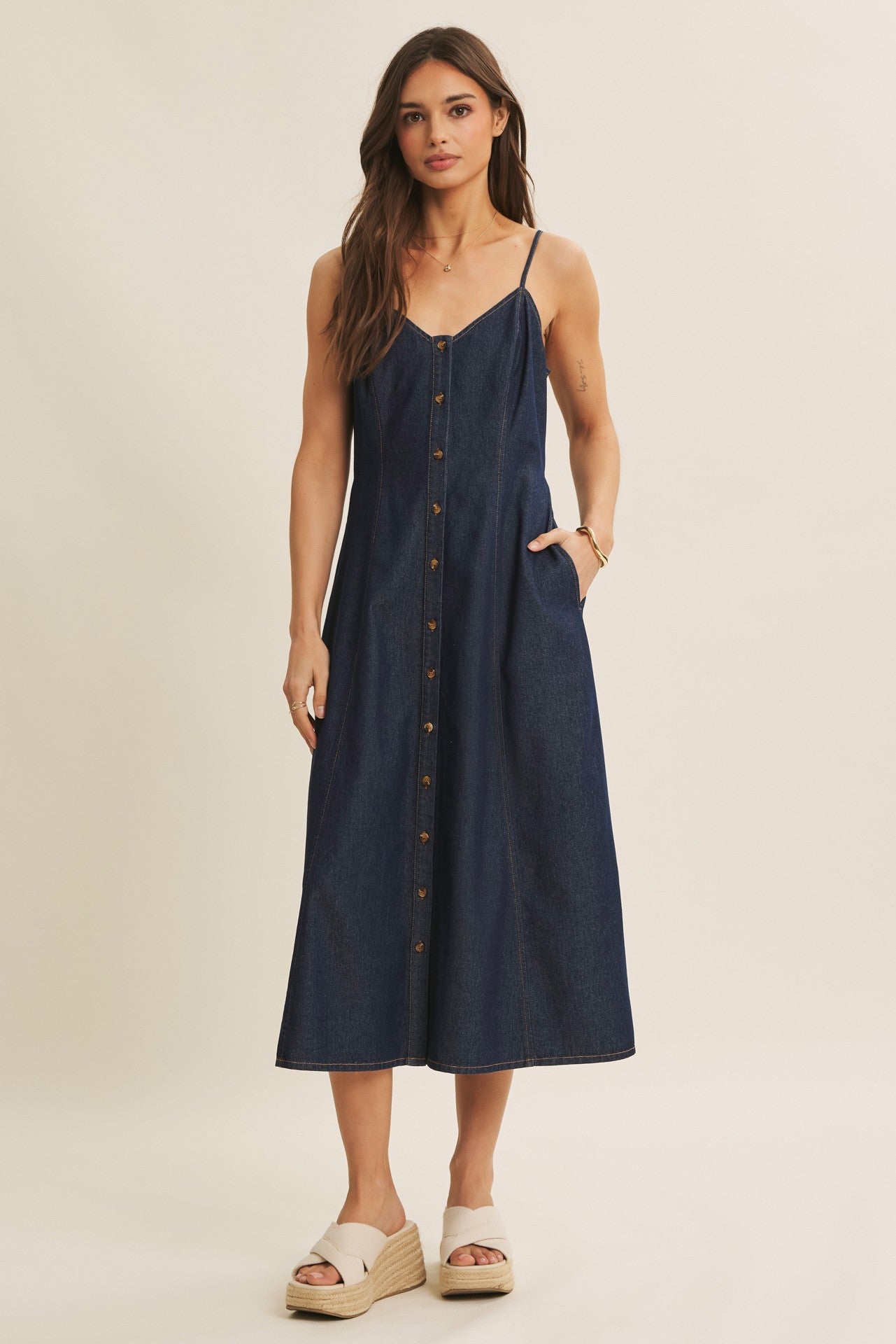woman wearing a navy blue denim button-up midi dress with thin straps and side pockets