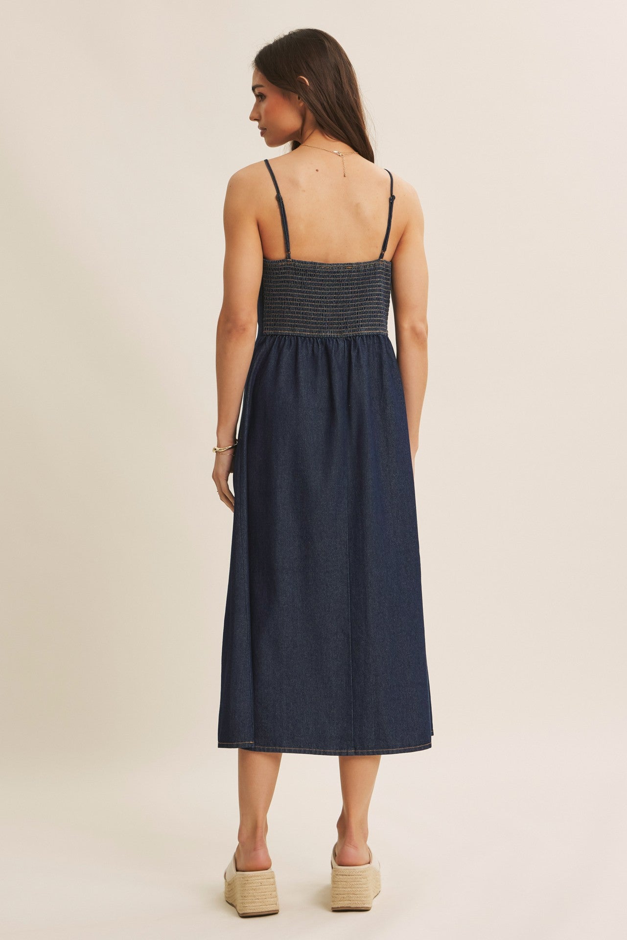woman wearing a back view of a dark denim maxi dress with spaghetti straps and a smocked bodice