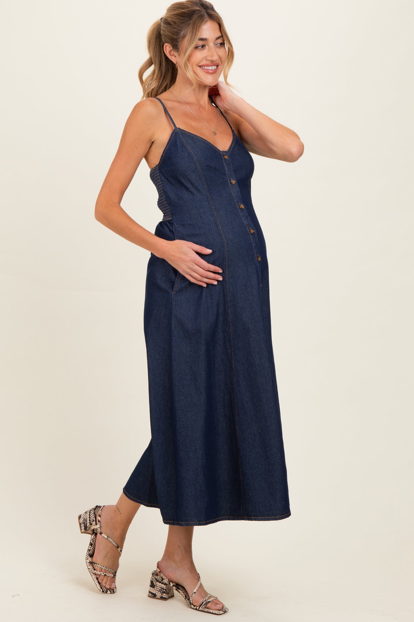 woman wearing a dark denim maternity dress with buttons and pockets, showcasing her baby bump