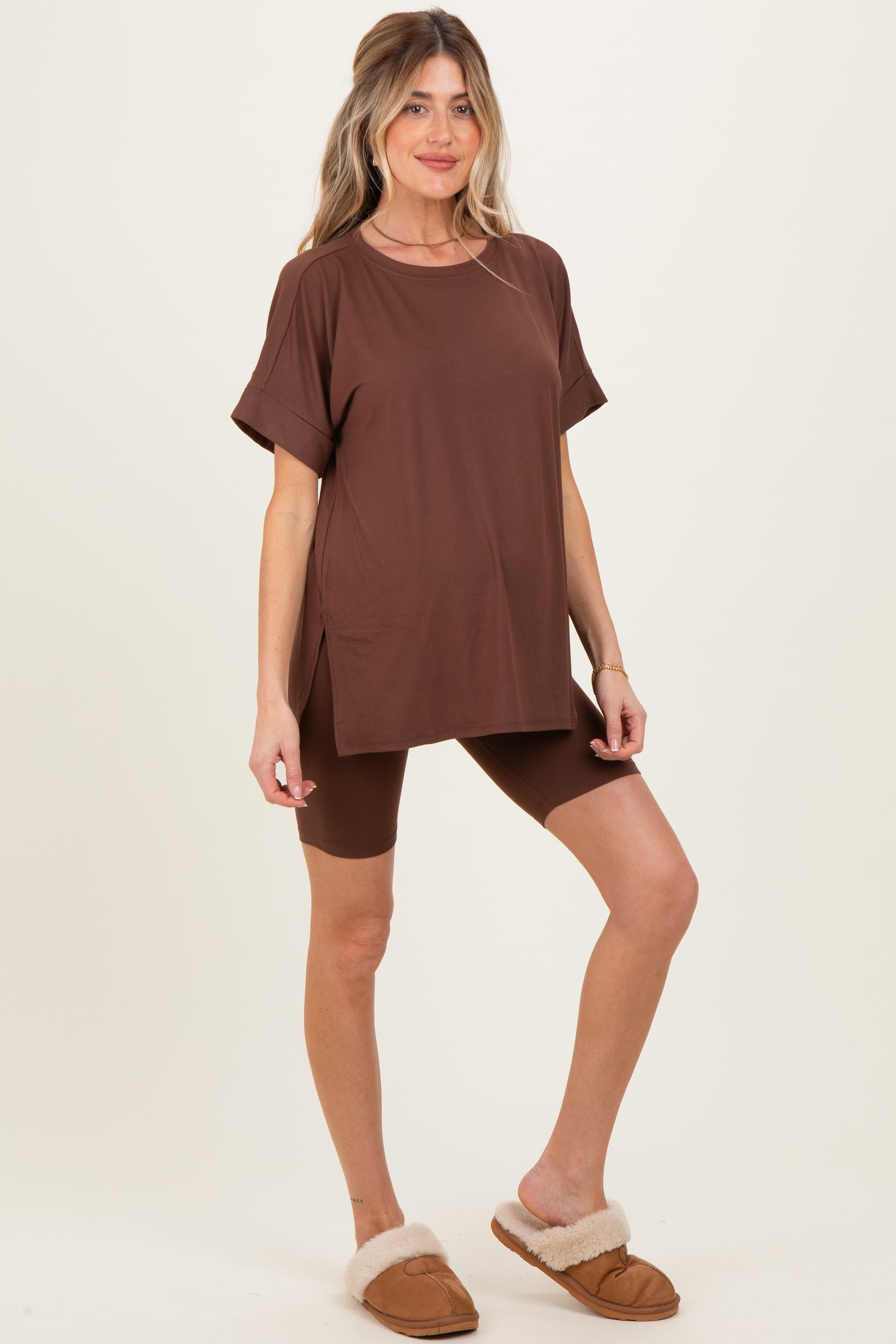 woman wearing a brown maternity t-shirt and matching bicycle shorts, standing in cozy slippers with a baby bump visible