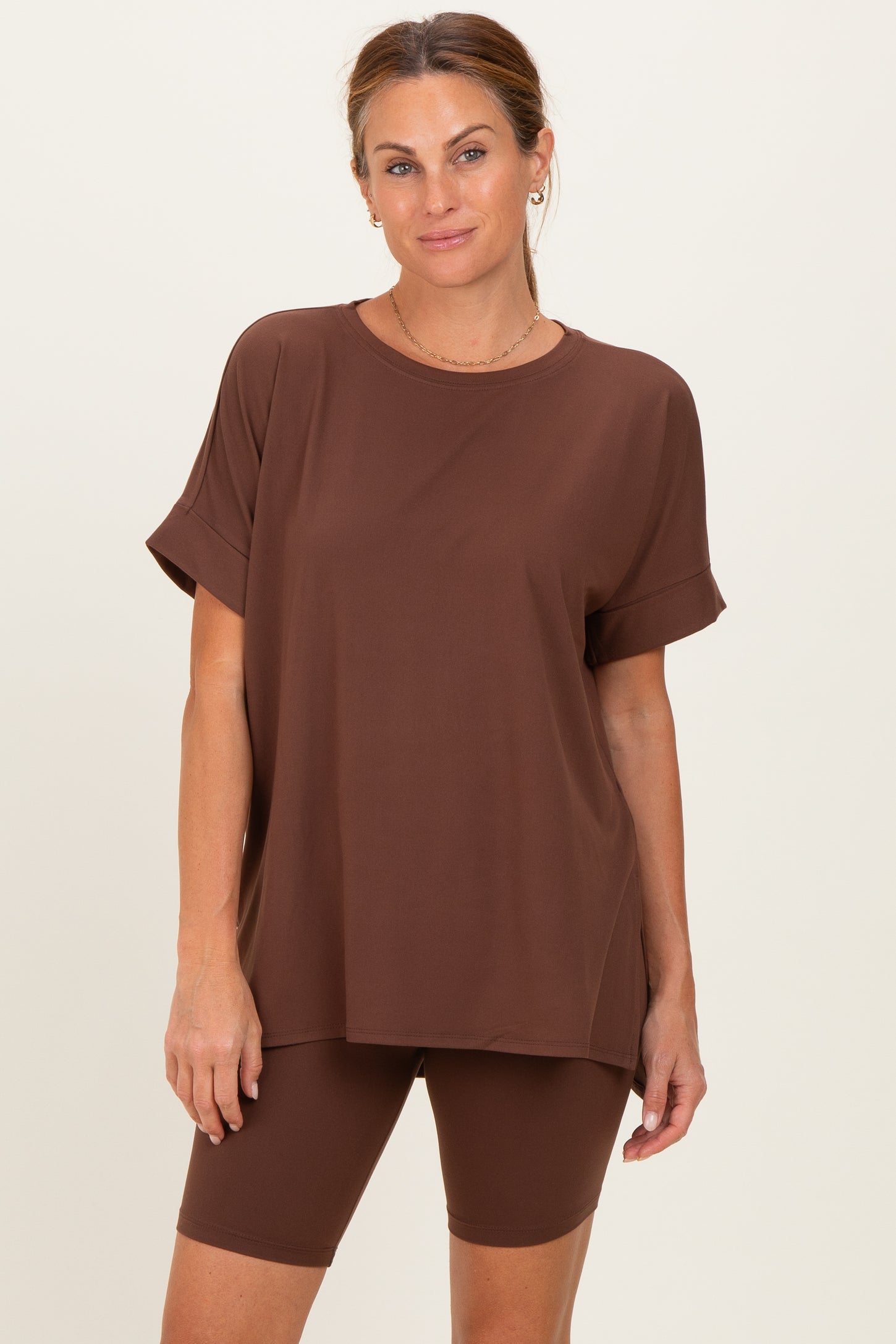 woman wearing a brown oversized t-shirt and matching bicycle shorts, standing against a neutral background