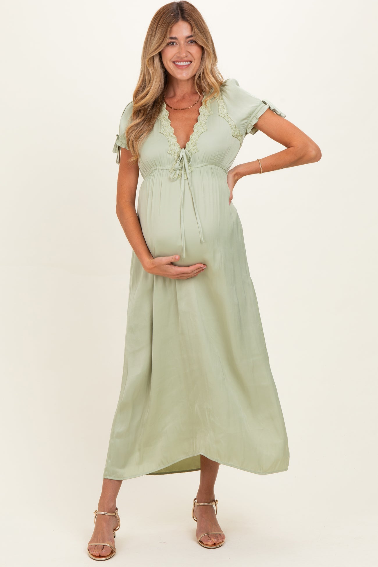 woman wearing a light green maternity dress with lace detailing and holding her baby bump