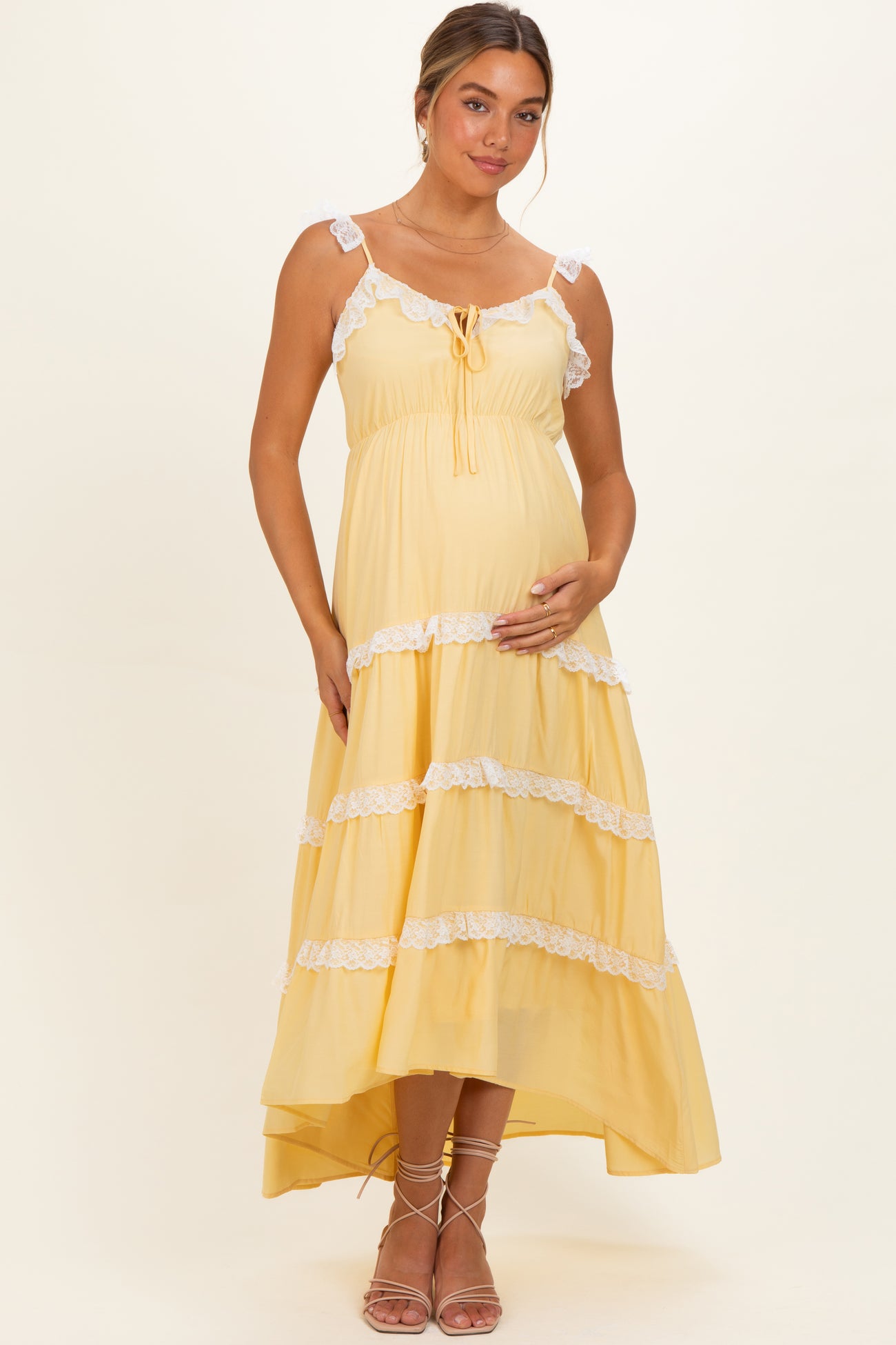 woman wearing a yellow tiered maternity dress with lace trim and a baby bump, standing gracefully