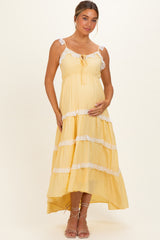 woman wearing a yellow tiered maternity dress with lace trim and a baby bump, standing gracefully