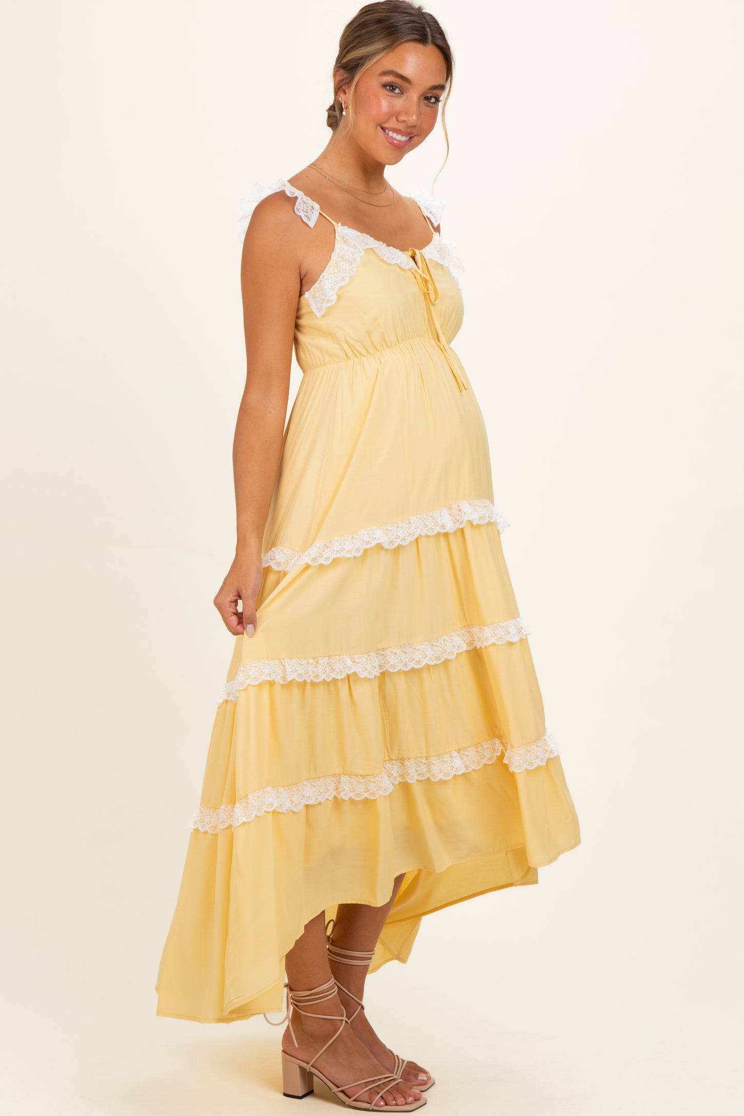 woman wearing a yellow maternity maxi dress with white lace trim and ruffled tiers, showing her baby bump