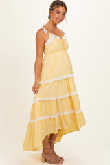 woman wearing a yellow maternity maxi dress with white lace trim and ruffled tiers, showing her baby bump