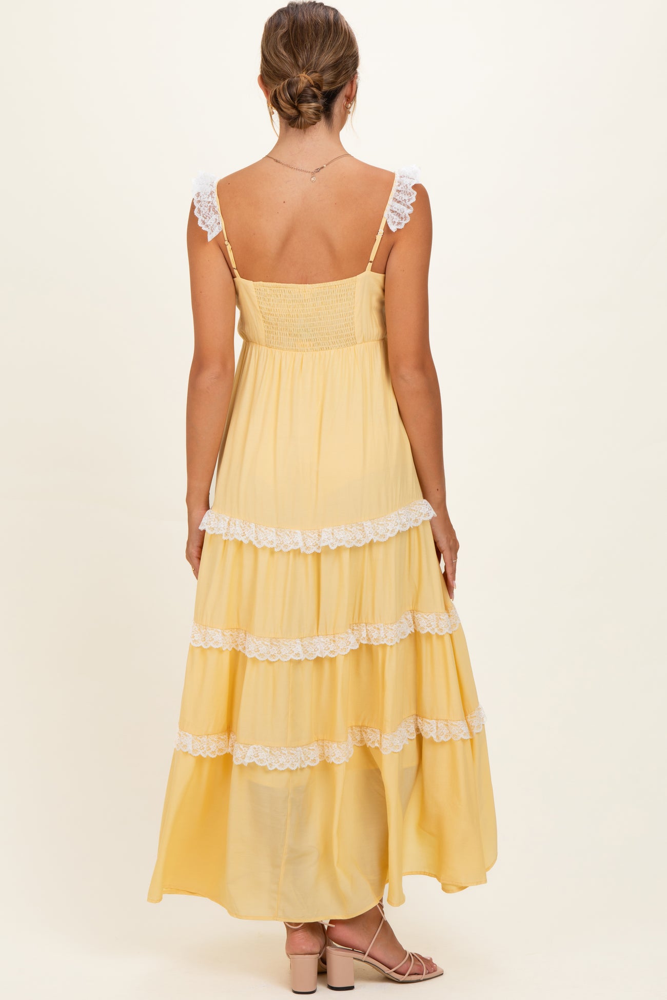 woman wearing a yellow maternity maxi dress with lace-trimmed tiers and a smocked bodice, showcasing her baby bump