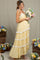 woman wearing a light yellow maternity maxi dress with lace trim, holding a bouquet of flowers and showcasing her baby bump